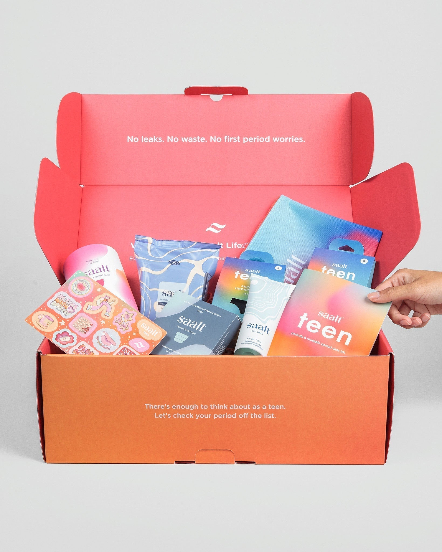 An open orange 'Saalt Teen' period starter kit box filled with various period care products and stickers.