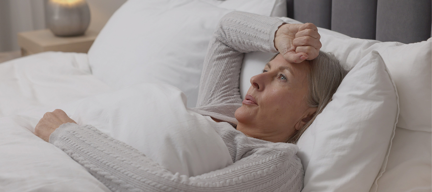 Woman lying awake in bed with hand on forehead, appearing restless or uncomfortable at night.
