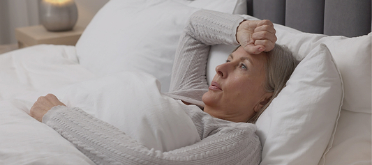 Woman lying awake in bed with hand on forehead, appearing restless or uncomfortable at night.