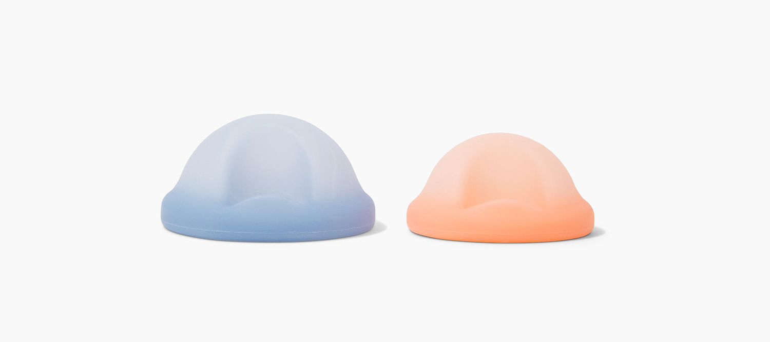 Two pastel silicone menstrual cups in blue and peach displayed on a light neutral background.
