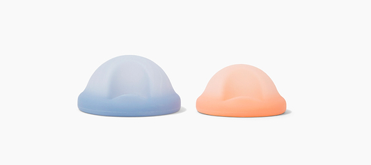 Two pastel silicone menstrual cups in blue and peach displayed on a light neutral background.