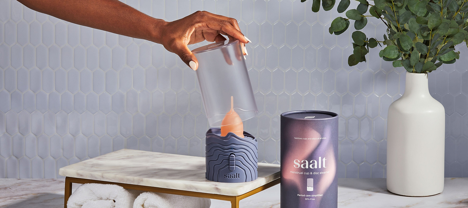 Hand placing a menstrual cup into a Saalt cup steamer on a bathroom counter.