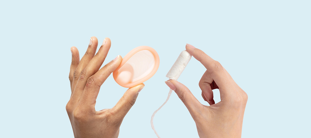 Two hands holding up period products: a peach-colored menstrual disc on the left and a white tampon on the right.