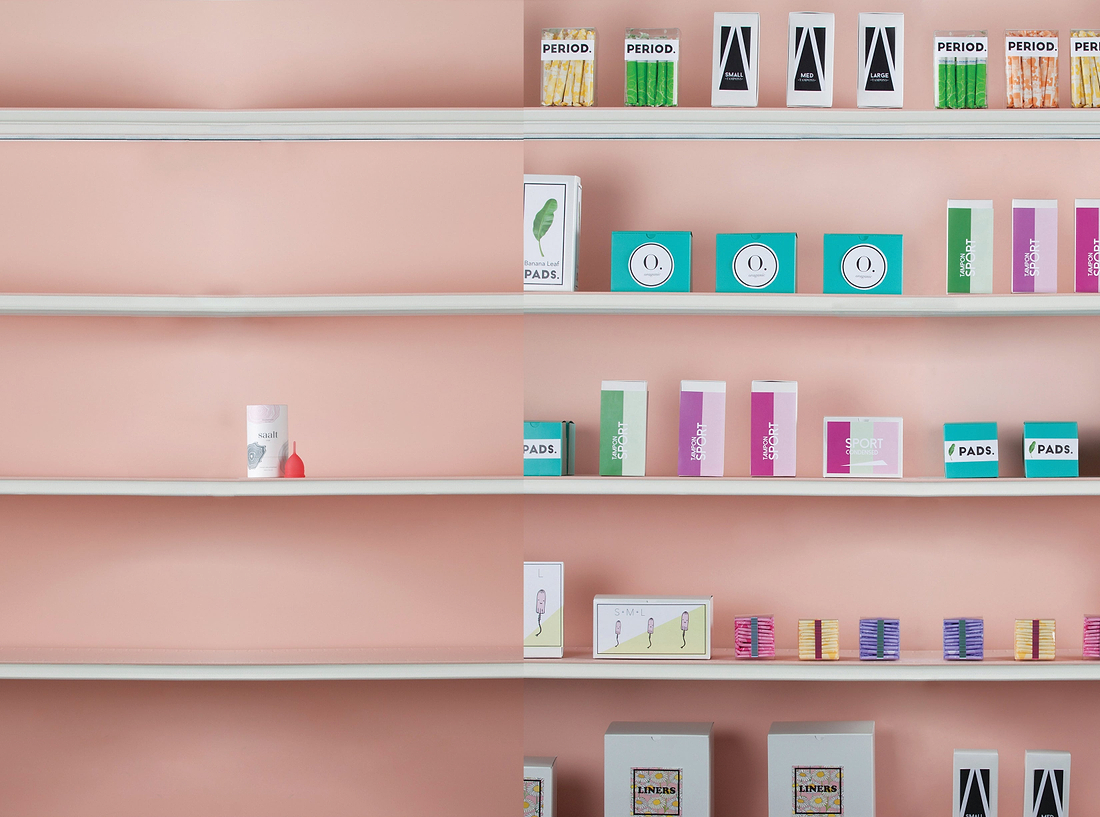 Shelves displaying assorted menstrual care products and packaging against a soft pink wall in a clean retail setting.