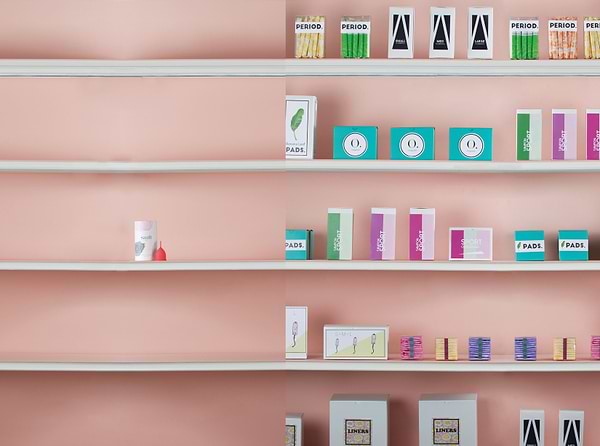 Shelves displaying assorted menstrual care products and packaging against a soft pink wall in a clean retail setting.