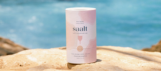 Saalt soft menstrual cup packaging displayed on rocks with a blurred blue water background.