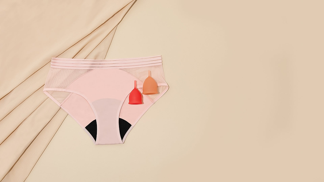 Pink period underwear with two menstrual cups on beige fabric background.