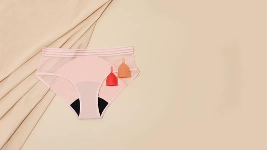 Pink period underwear with two menstrual cups on beige fabric background.