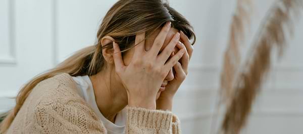 A woman sits with her face in her hands, appearing stressed, overwhelmed, anxious, or emotionally exhausted.