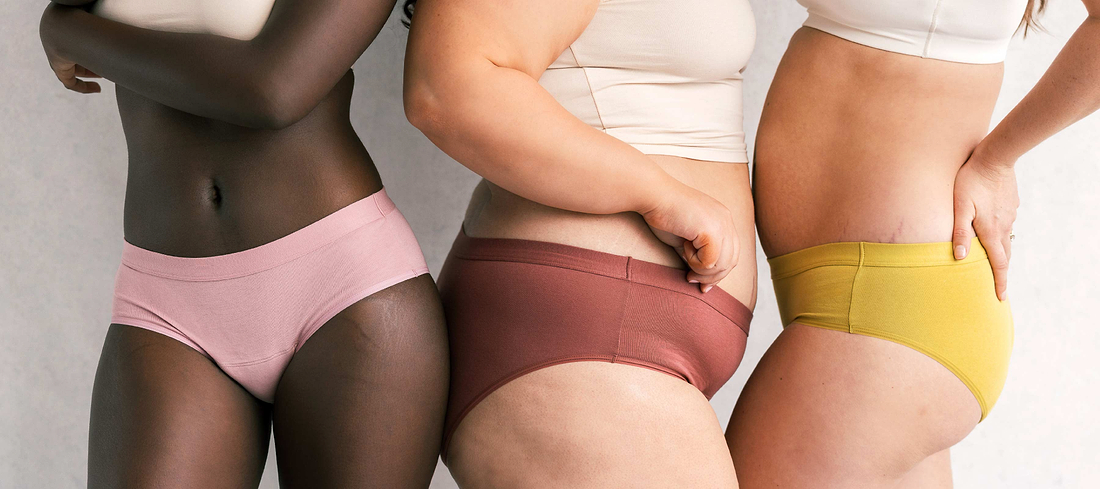 Three women in colorful period underwear posing together to showcase inclusive sizing and body diversity.