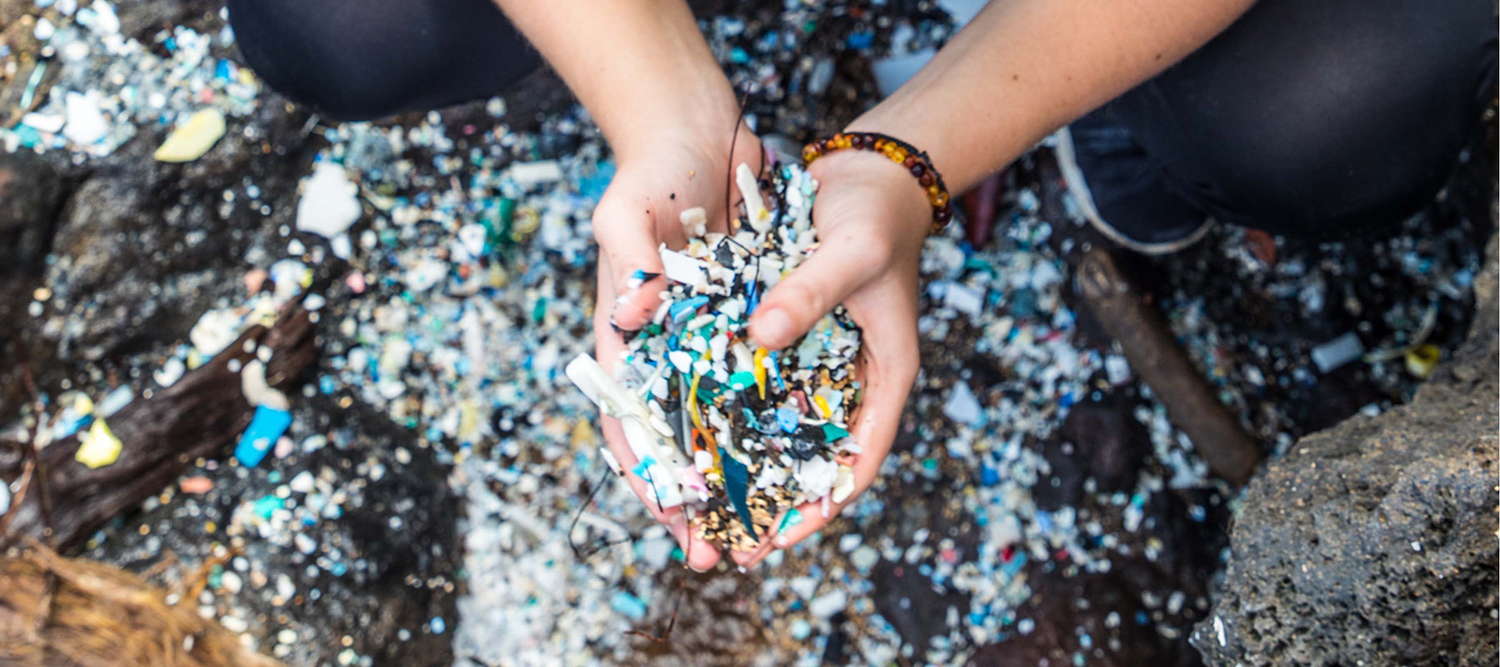 Hands holding plastic waste and microplastics collected from a polluted shoreline.