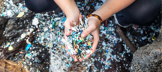 Hands holding plastic waste and microplastics collected from a polluted shoreline.