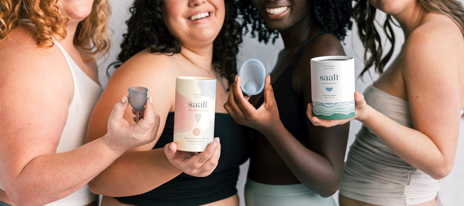Group of women holding Saalt menstrual cups, disc, and product packaging while smiling together.