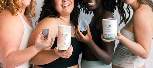 Group of women holding Saalt menstrual cups, disc, and product packaging while smiling together.