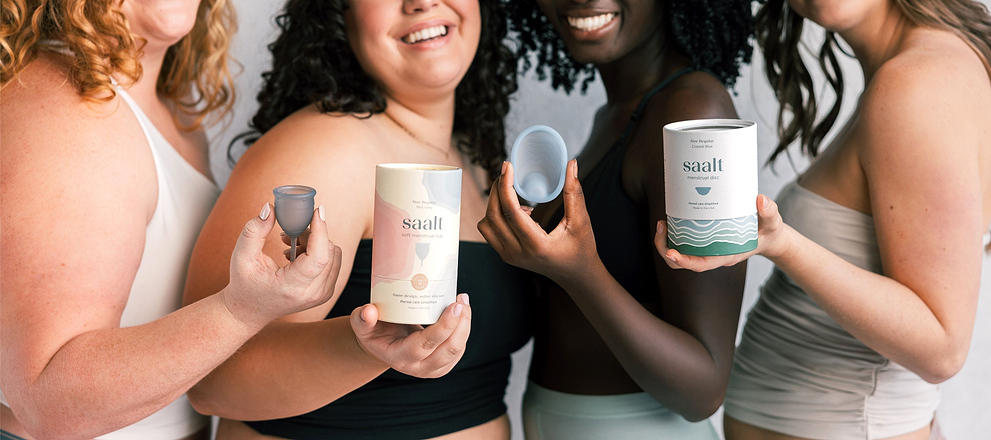 Group of women holding Saalt menstrual cups, disc, and product packaging while smiling together.