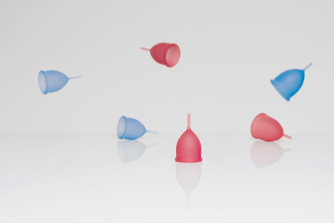 Pink and blue menstrual cups floating and resting on a white reflective surface against a light background