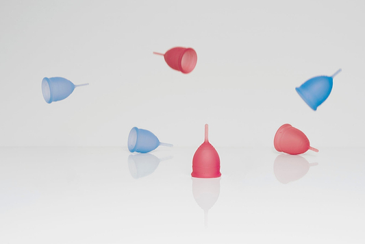Pink and blue menstrual cups floating and resting on a white reflective surface against a light background