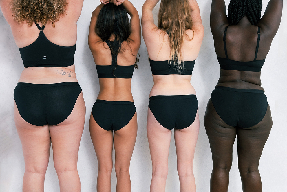 Four women with diverse body types and skin tones wearing black underwear, standing side by side from the back.