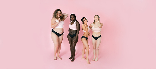 Four women of diverse body types and skin tones pose confidently in matching black underwear against a pink background.
