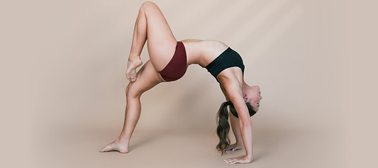  Woman in athletic wear performing a backbend yoga pose against a neutral studio background.