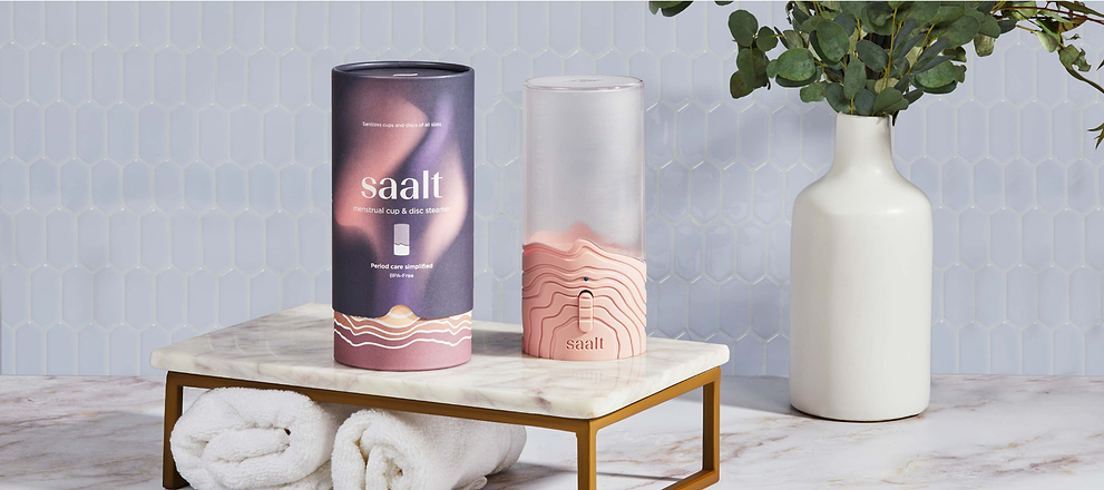 Saalt menstrual cup steamer and packaging displayed on a marble bathroom counter beside a white vase.