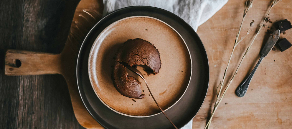 Top view of a rich chocolate dessert on a plate with a spoon on a rustic table.