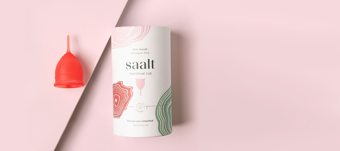 Pink Saalt menstrual cup beside branded packaging on a soft pink background.