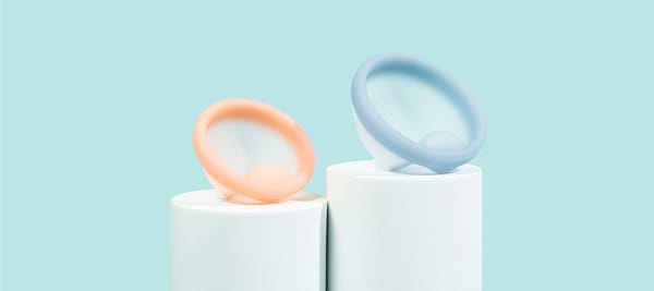 Two reusable menstrual discs displayed on white stands against a light blue background.
