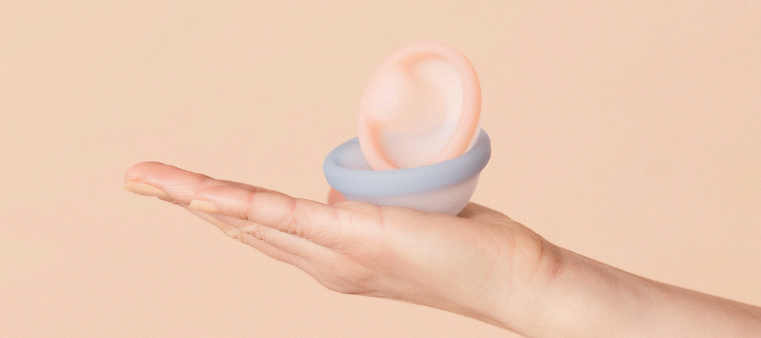 Hand holding pastel menstrual discs against a soft beige background.