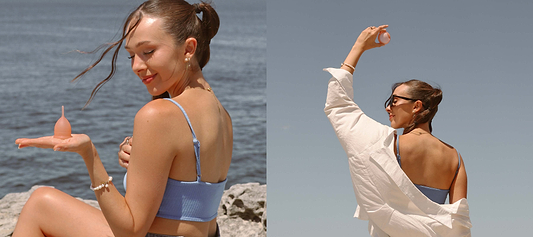 Woman by the water holding a pink menstrual cup, posing under sunny skies.