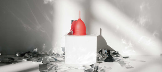 Red menstrual cup displayed on a white pedestal with reflective shards and dramatic lighting.