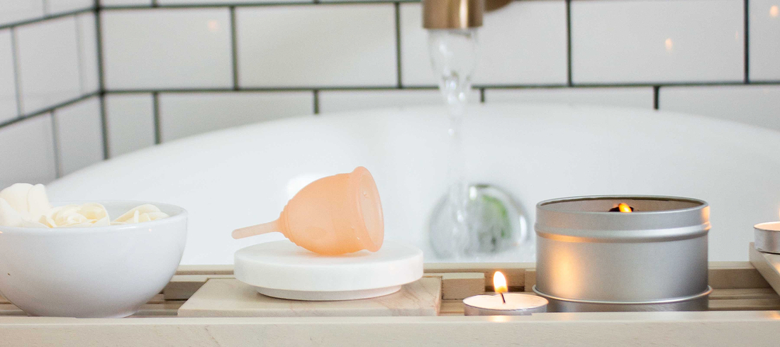 Menstrual cup displayed beside candles and bath items in a calm bathroom setting.
