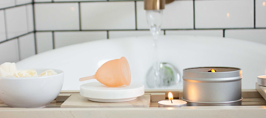 Menstrual cup displayed beside candles and bath items in a calm bathroom setting.