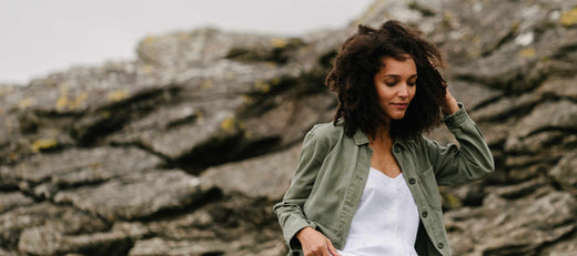 Woman with curly hair wearing a green jacket outdoors near rocky terrain.