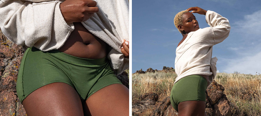 Model outdoors wearing green period shorts and cream sweatshirt in rocky grassland setting.