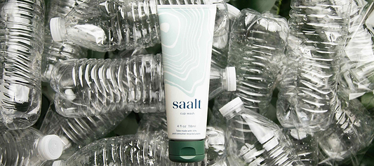 Menstrual cup wash tube surrounded by recycled plastic bottles.