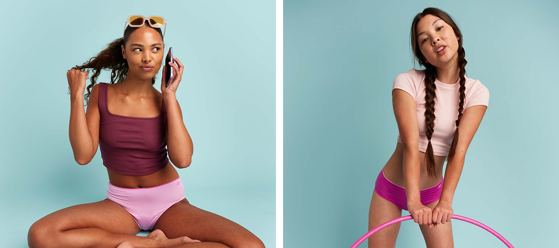 Two women modeling colorful underwear and casual tops against a pastel blue studio background.