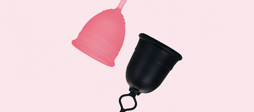 Pink and black menstrual cups suspended against a light background.