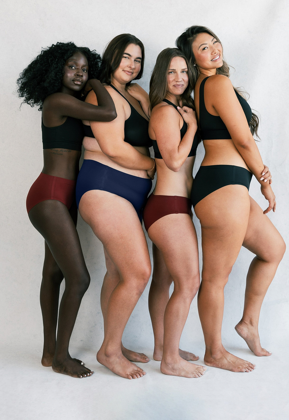 Diverse group of women posing confidently in underwear against a neutral studio background.