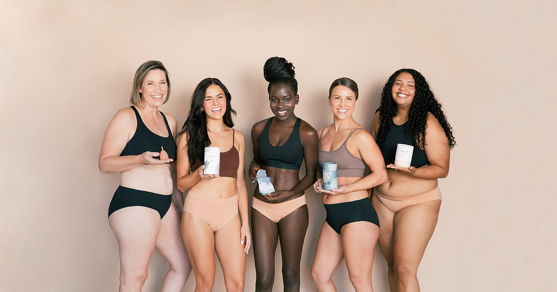 Five women in underwear smiling and holding menstrual care products against a neutral backdrop.