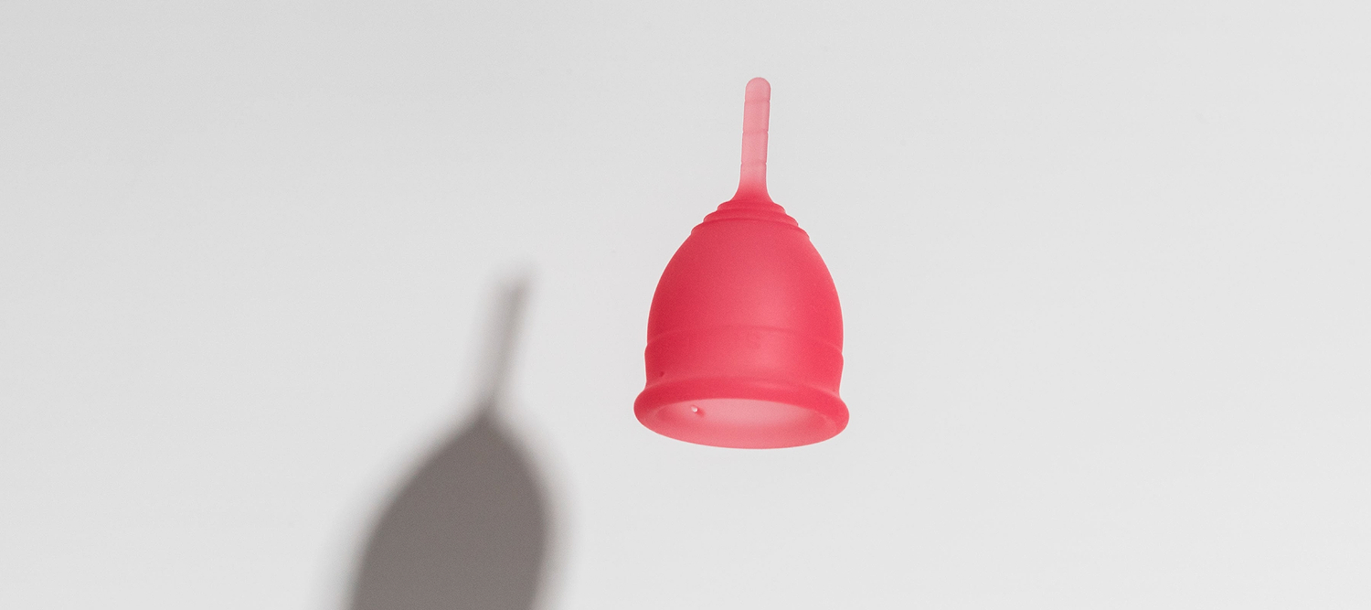 Pink menstrual cup floating against a light background with a soft shadow below.