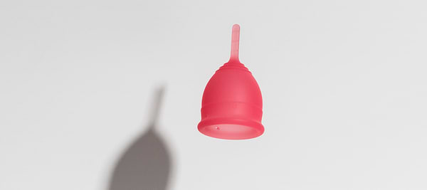 Pink menstrual cup floating against a light background with a soft shadow below.