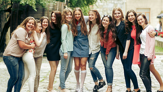 Group of smiling young women posing together outdoors on a cobblestone street.