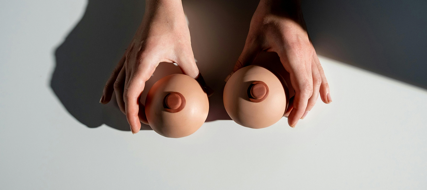 Hands holding two breast-shaped models on a table, suggesting breast health or self-exam concept.
