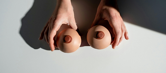 Hands holding two breast-shaped models on a table, suggesting breast health or self-exam concept.