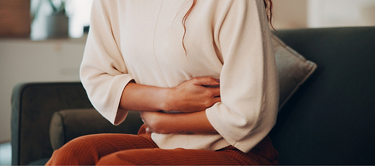 Person sitting on a couch holding their abdomen, appearing uncomfortable.