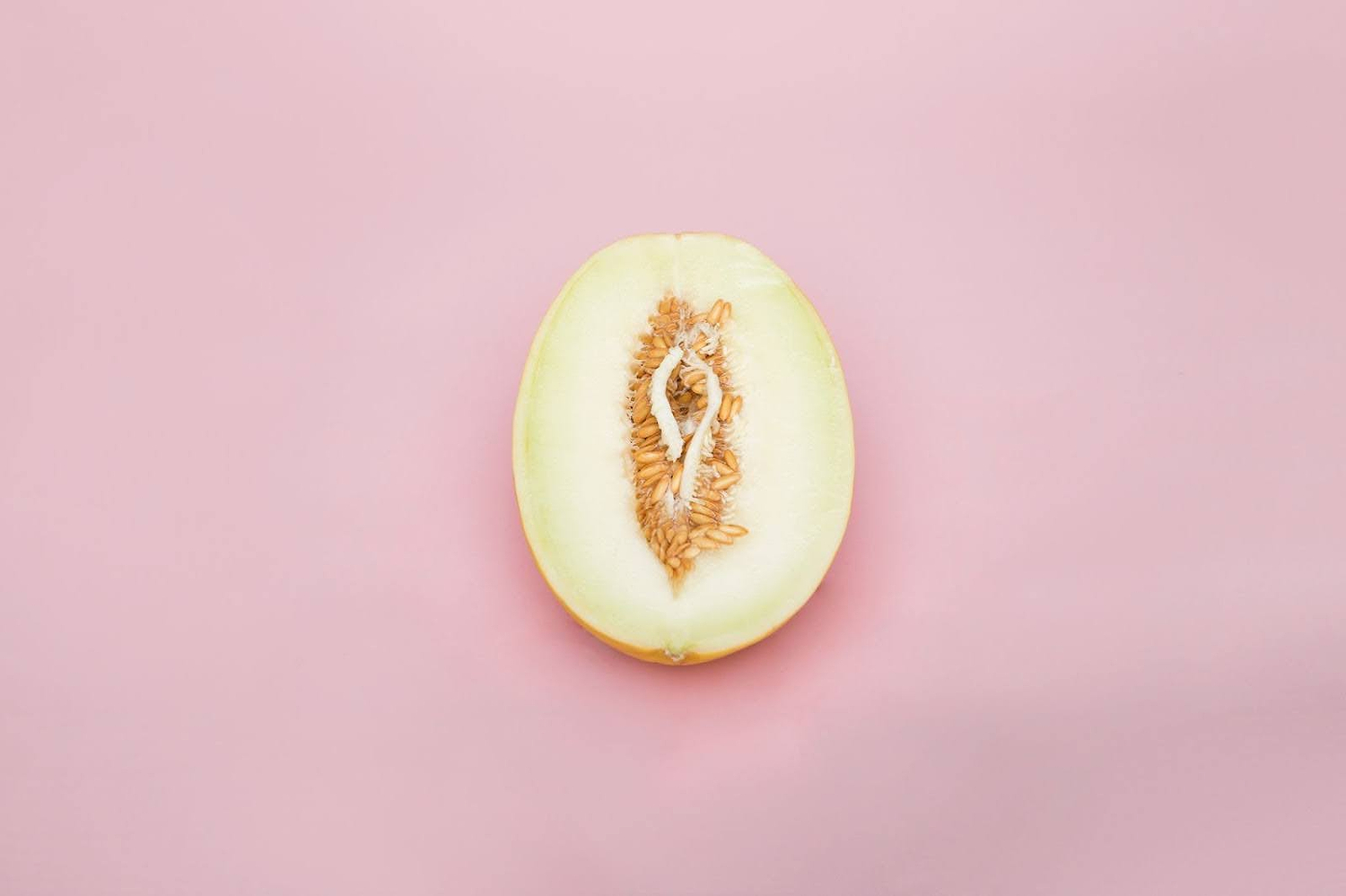 Half cantaloupe melon on pink background, styled to resemble female anatomy.
