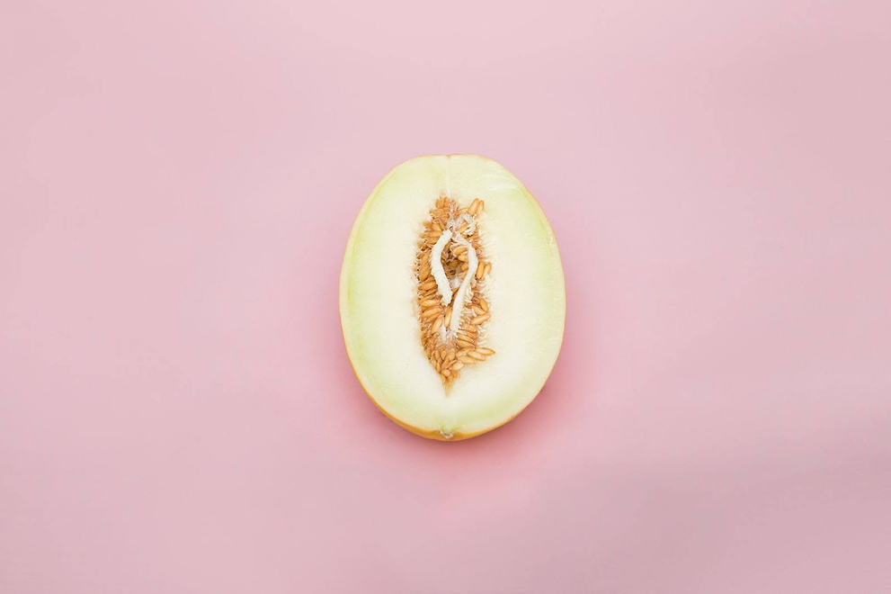 Half cantaloupe melon on pink background, styled to resemble female anatomy.