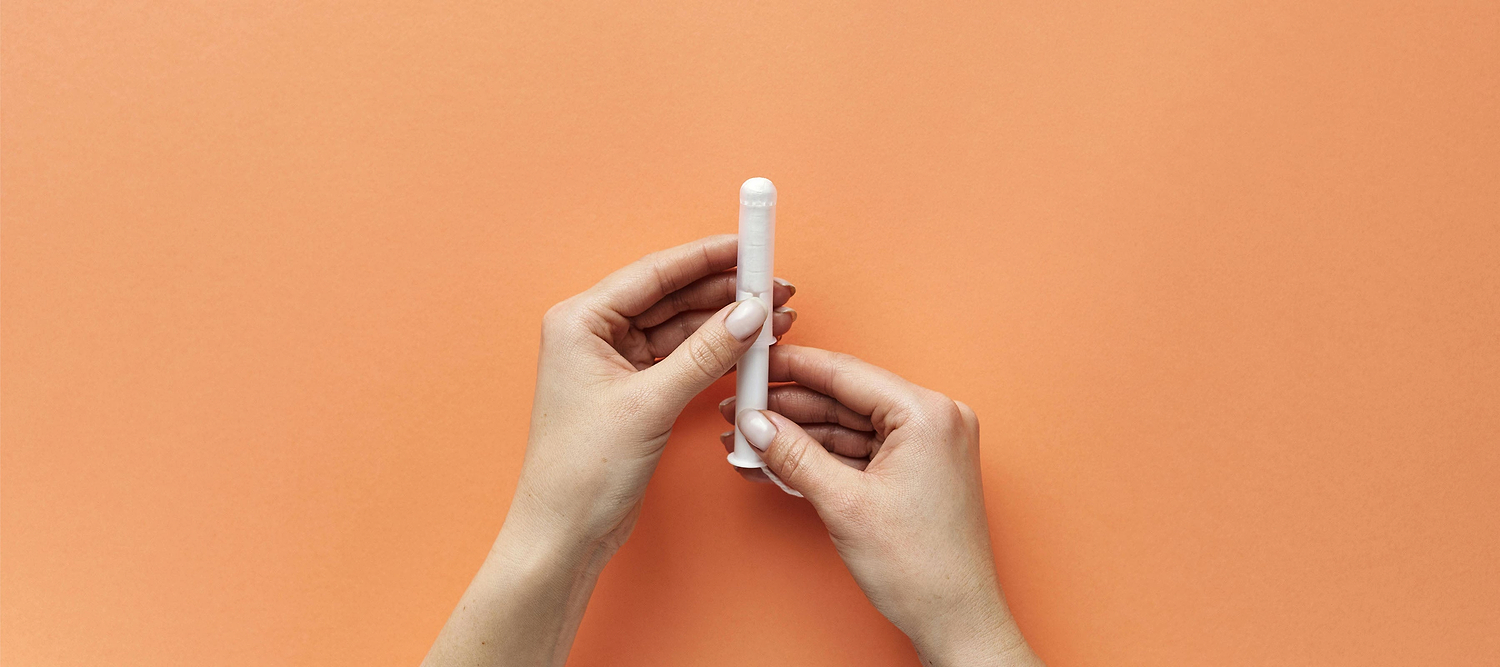 Hands holding a tampon against an orange background