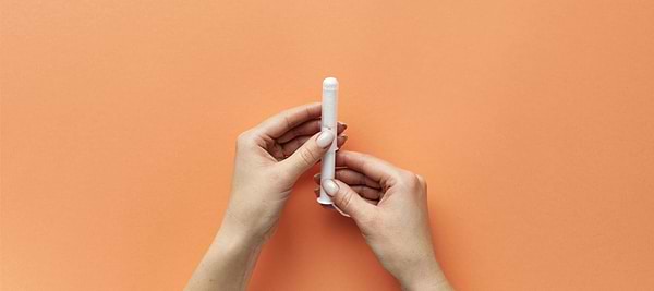 Hands holding a tampon against an orange background
